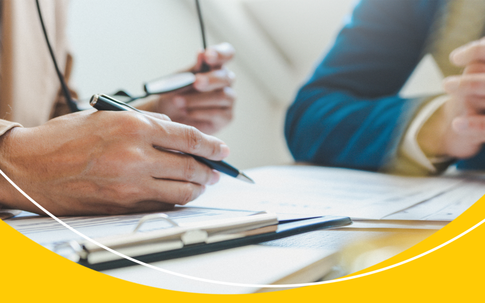 Side view of a person holding their glasses in their hand while writing on a document