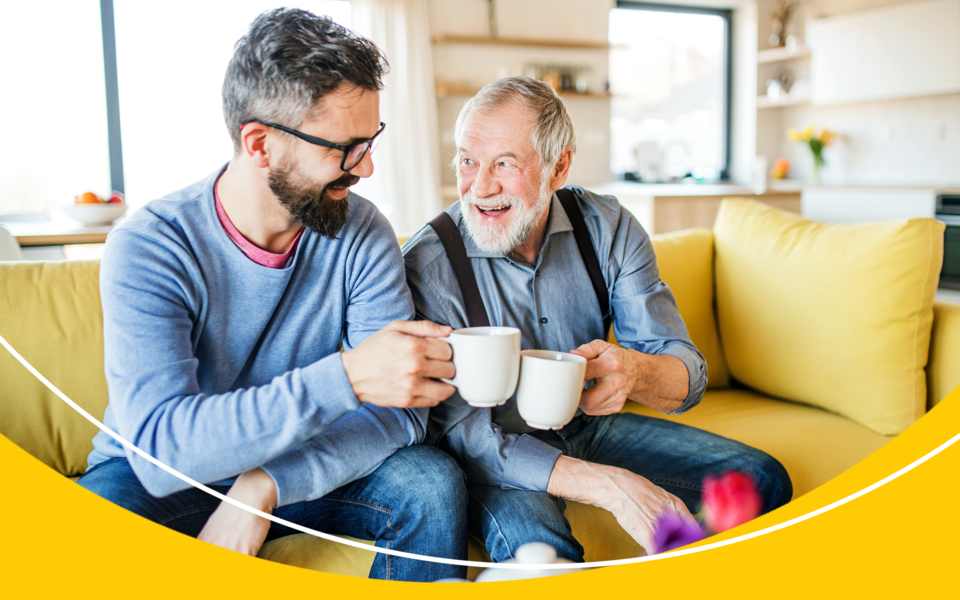 A man smiling and sharing a cup of coffee with an older gentlemen