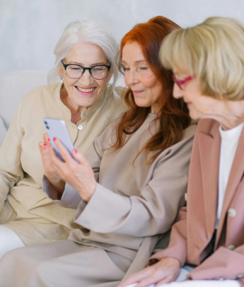 Three elderly women smiling and looking at a phone