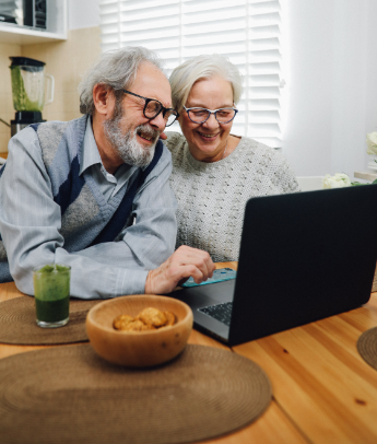 An elderly couple smiling and browsing on a laptop