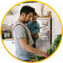 A father working in the kitchen while holding his baby boy