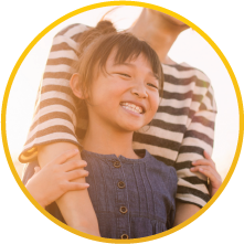 A girl smiling and being embraced by her mother from behind