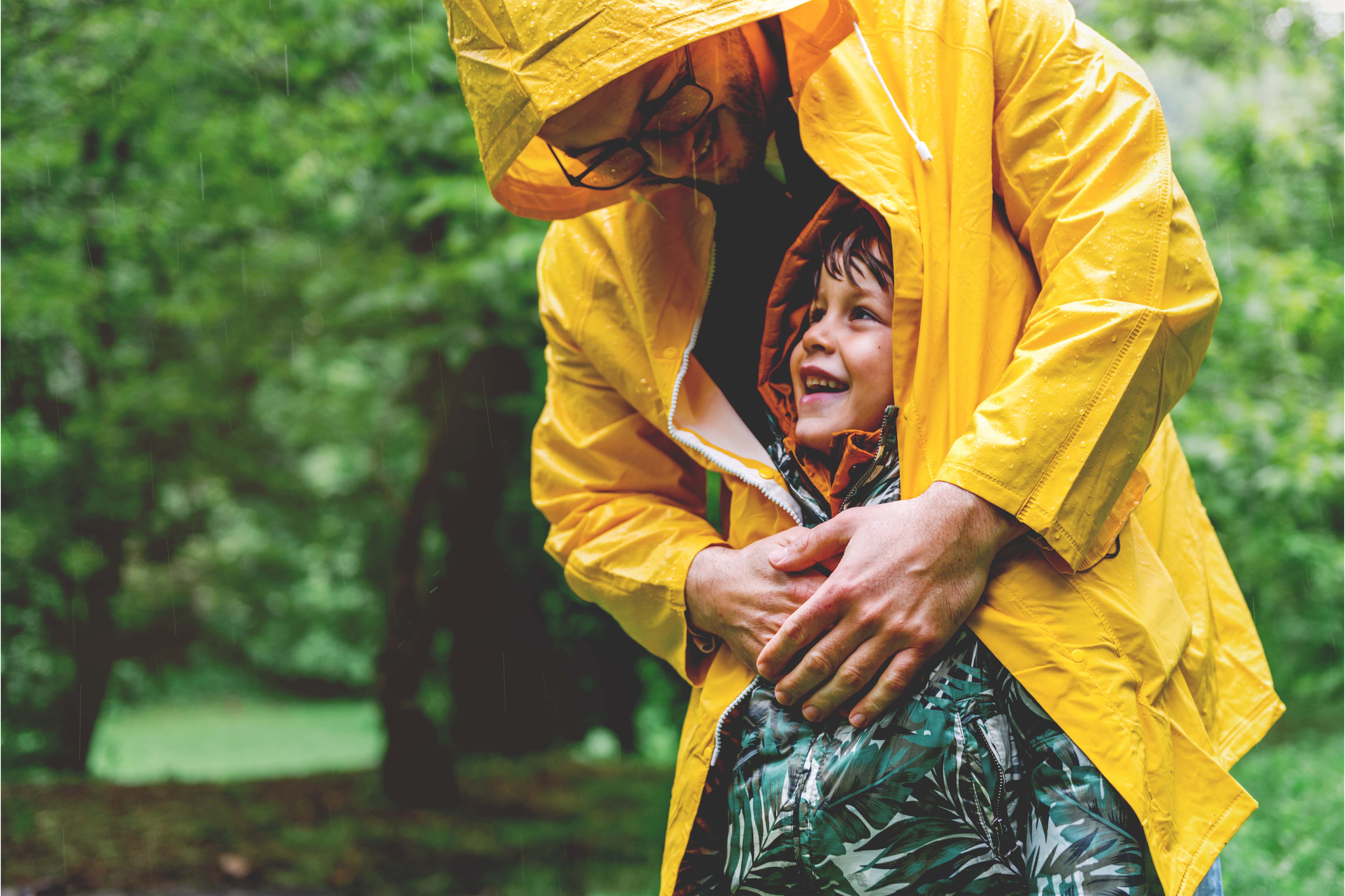 A father and his son enjoying the rains and wearing raincoats