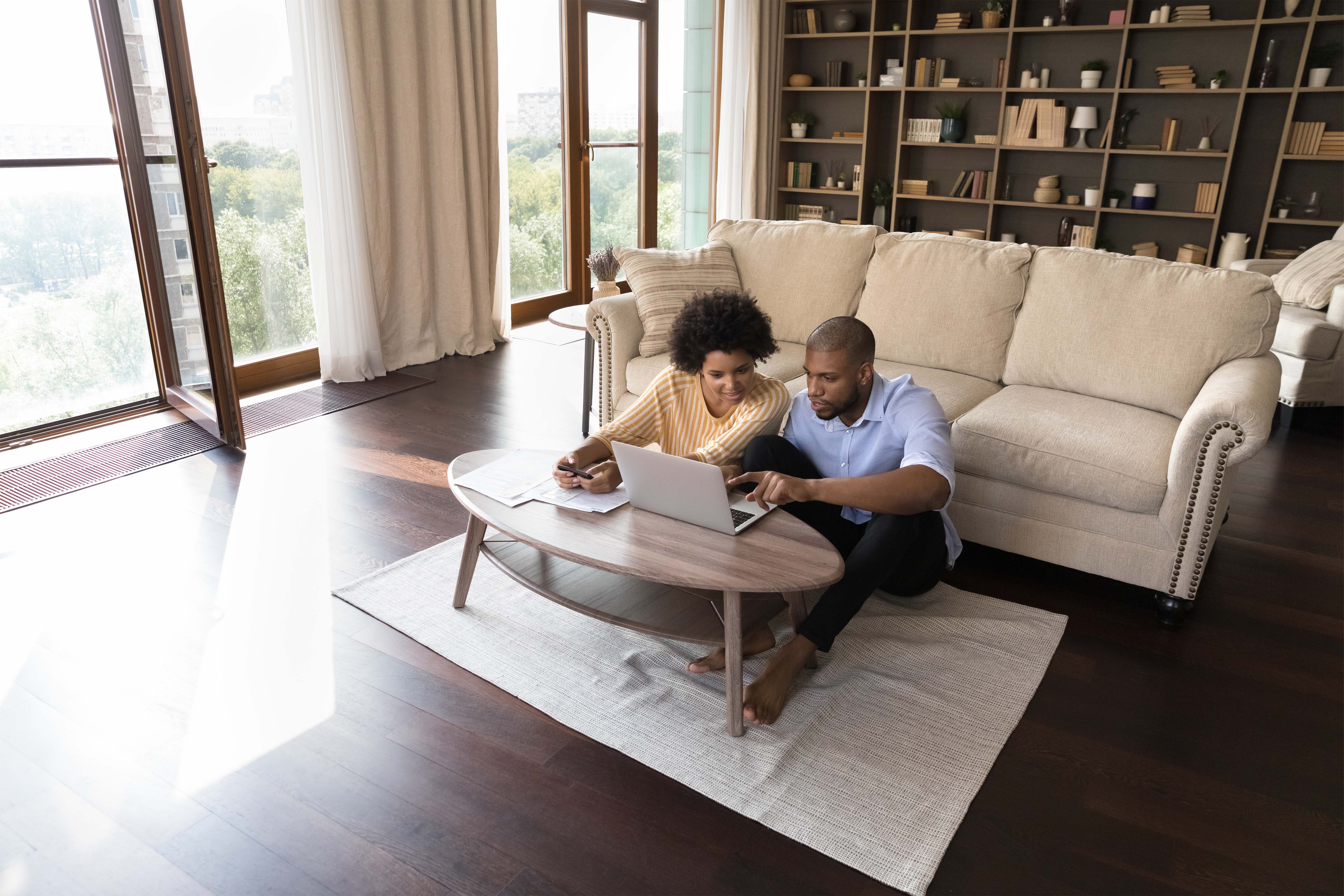 A young couple sitting on the floor in the living room and discussing while using their laptop