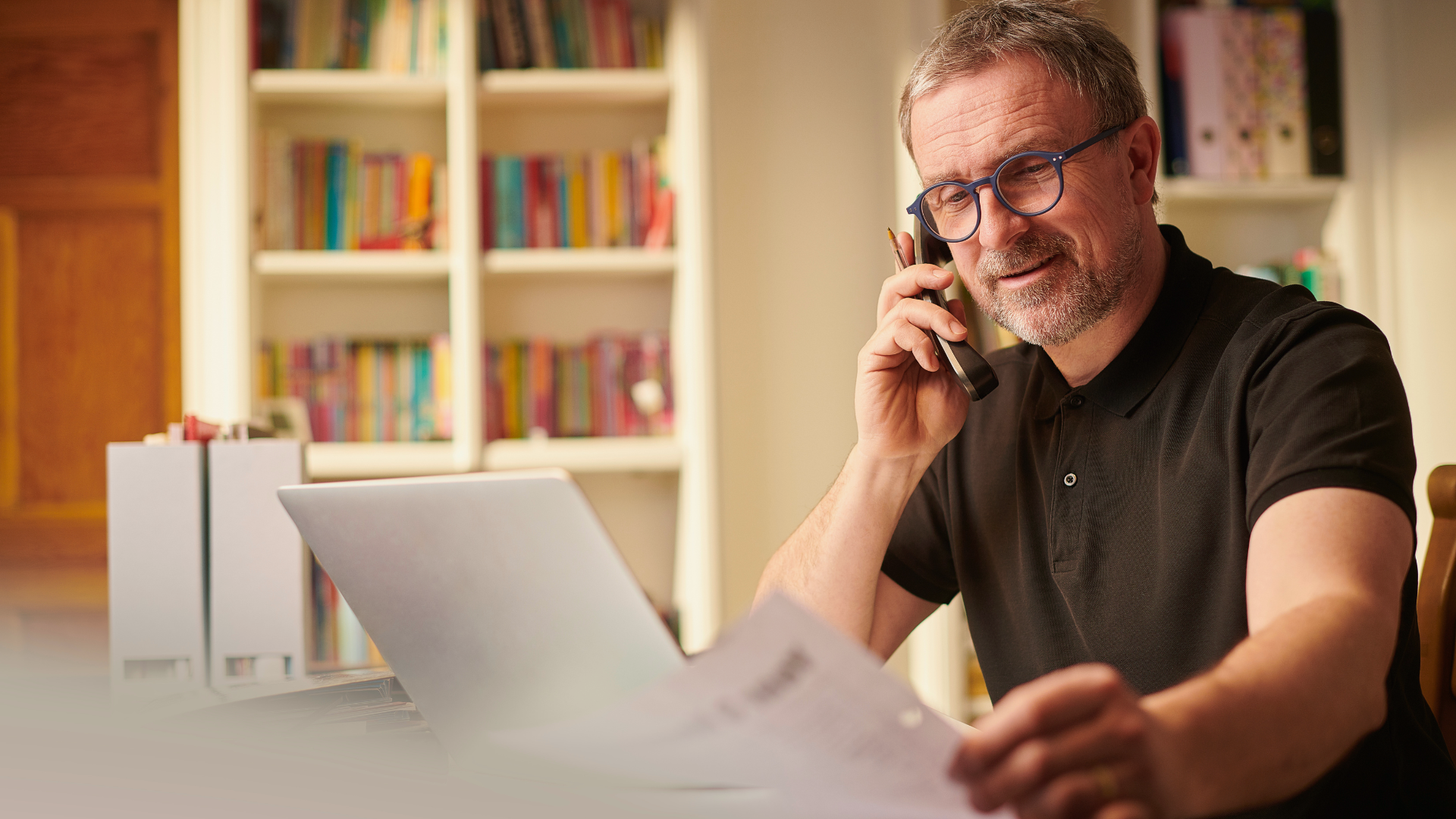 Man on phone loking over papers at a computer