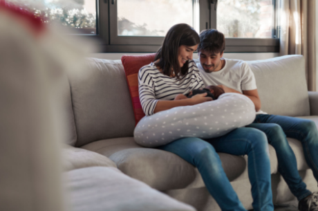 Young couple sitting on a couch, smiling and looking at their newborn baby.