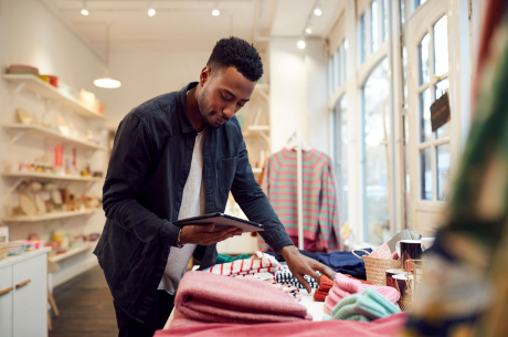 Man in a black jacket using a tablet in a store with various items displayed on a table.