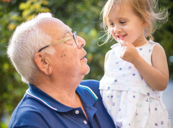 Elderly man holding his granddaughter and staring at her as she smiles