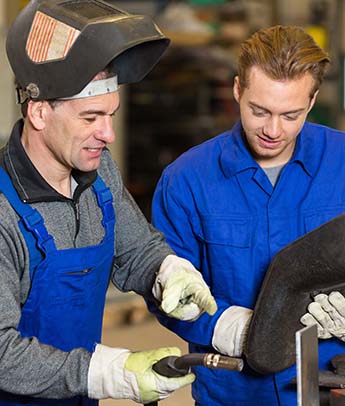 Instructor teaching trainee how to weld metal