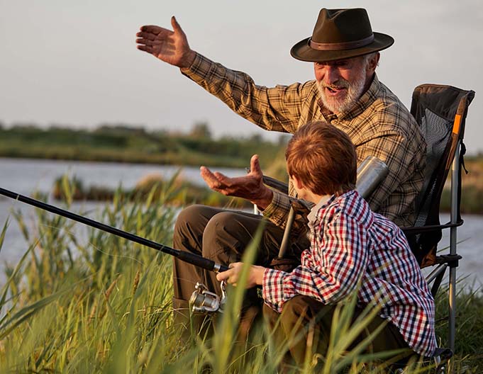Grandfather and boy fishing at sunset on river in the countryside