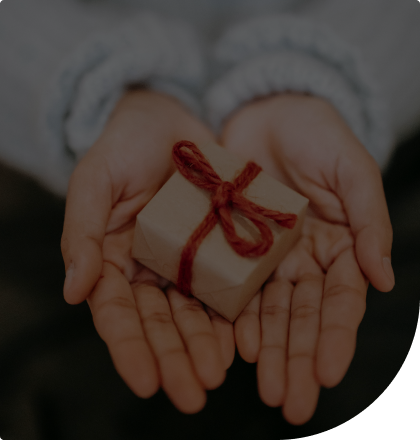 A photo of someone holding a small brown box wrapped with red ribbon.