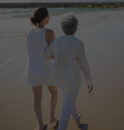 Two women walking arm-in-arm down a beach.